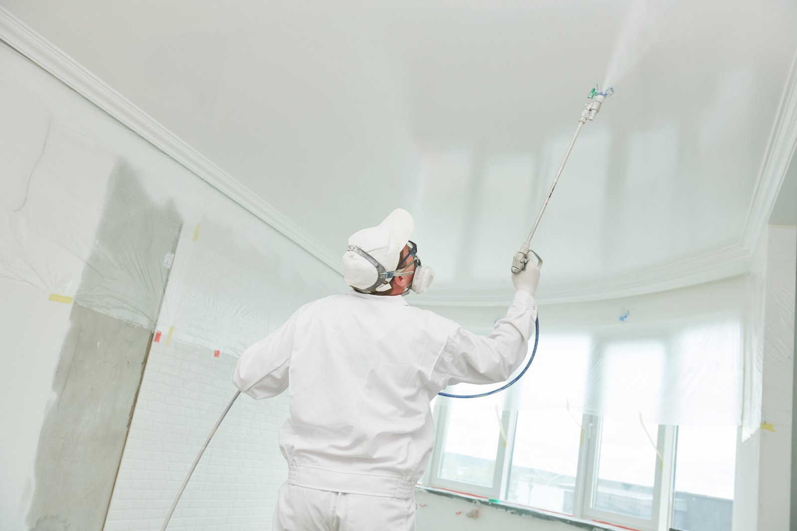 Airless spray painting. Painter worker with sprayer jet painting ceiling surface into white color at home impovement and refurbishment